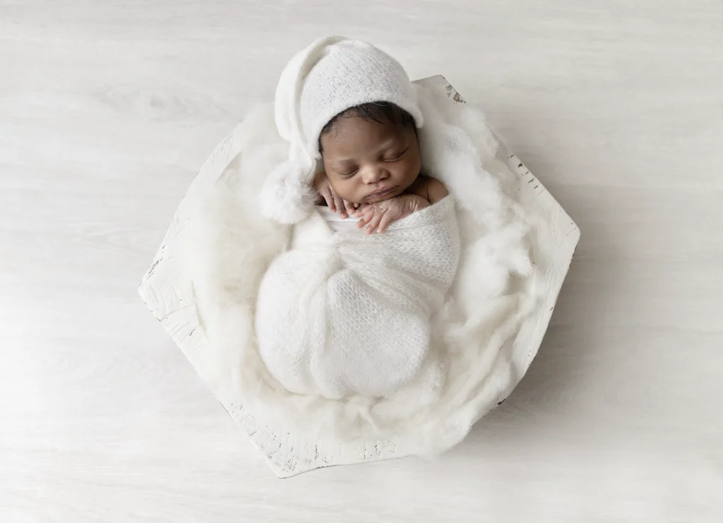 Photo d'un nouveau né dans un bol sur un tapis de laine très doux. Enveloppé dans un cocon en laine portant un bonnet lutin lors d'une séance photo par Tiana Photographe naissance Toulouse
