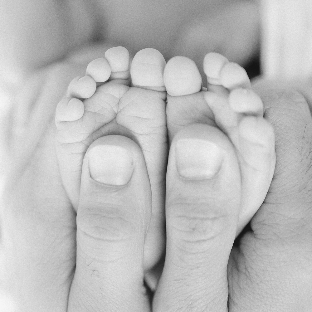 Photo des petits pieds dans les mains de son papa lors d'une séance photo avec Tiana Photographe Toulouse