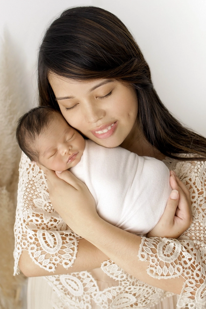 Photo d'une maman portant son bébé dans ses bras tendrement lors d'une séance photo avec Tiana Photographe Toulouse