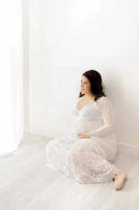 Photo d'une maman enceinte assise à côté d'une fenêtre lors d'une séance photo au studio de Tiana Photographe Toulouse