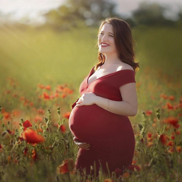 Photo d'une future maman au coucher du soleil dans un champs de coquelicot