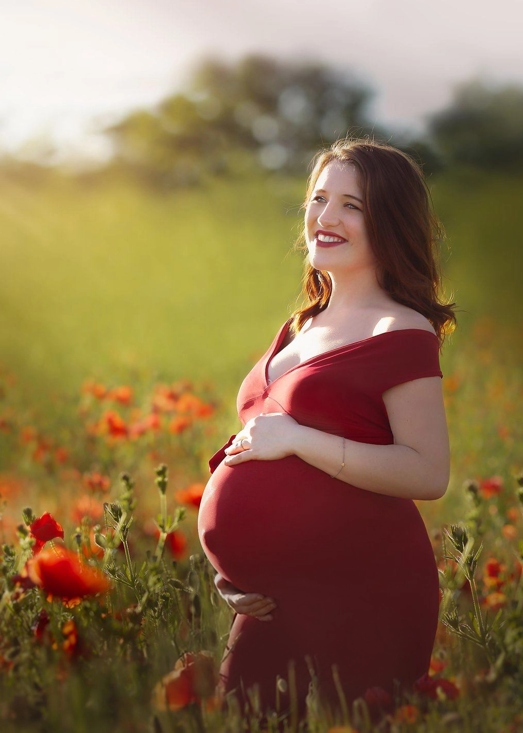 Photo d'une future maman au coucher du soleil dans un champs de coquelicot