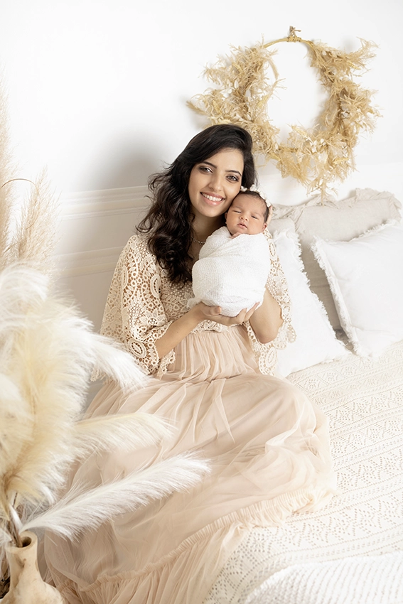 Photo d'une maman qui tient son bébé sur un lit lors d'un shooting nouveau né avec Tiana Photographe Toulouse